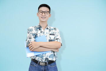 A cheerful young Asian man wearing glasses and batik shirt, standing and smiling confidently while...