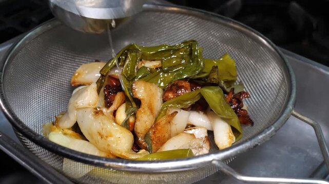 The rendered mixture of golden-brown pork fat, onions, garlic, and green onions is meticulously strained from a wok using a ladle and fine-mesh sieve.