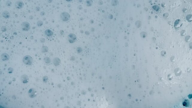 Bubbles of white soap foam. Moving Soap foam popping bubble on a blue backdrop. Soap sud macro structure. Clean, cleaning concept, laundry, shower. . High quality 4k footage