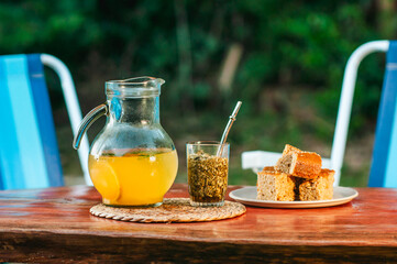 Jarra de vidrio con jugo de naranjas y menta al lado de un Tereré con yerba mate sobre la mesa en...
