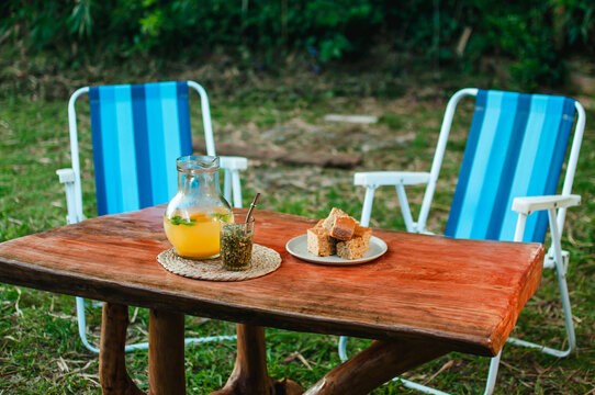 Un terer&eacute; de jugo de frutas con bocadillos sobre una mesa r&uacute;stica y silletas azules en el c&eacute;sped, momento de descanso al aire libre.