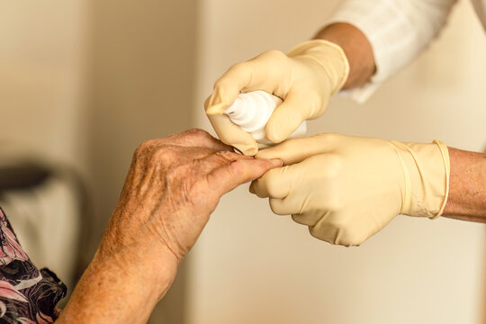 A home care nurse provides wound care to an elderly woman&rsquo;s finger during an in-home medical visit.