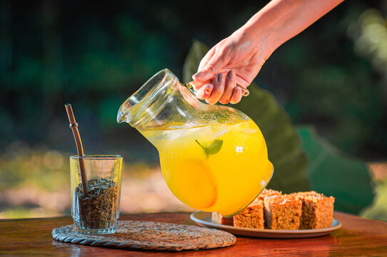 Mano de mujer sirviendo jugo de naranja con menta en un vaso de Terer&eacute;, bebida fr&iacute;a tradicional del Paraguay y Misiones, tarde de verano al aire libre.