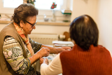Fototapeta premium An elderly woman folds dish towels at her kitchen table, managing everyday household tasks.