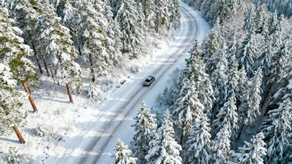 Aerial view of a car driving on a snowy road through a winter forest