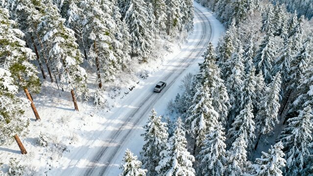 Aerial view of a car driving on a snowy road through a winter forest - Powered by Adobe