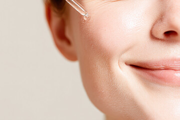 Obraz premium A close-up of a smiling woman's face applying skincare serum, highlighting healthy, glowing skin and a radiant complexion.