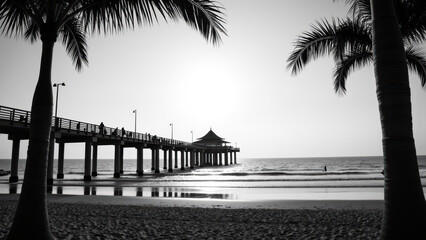 Serene beach scene featuring pier extending into ocean, framed by palm trees. sun sets in background, casting tranquil glow over water