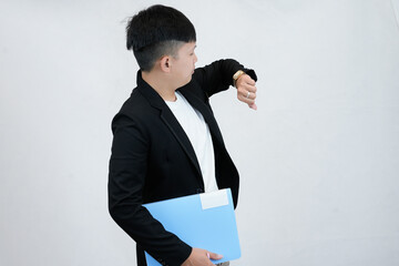 Busy Asian male professional or businessman in a black suit checking his wristwatch while holding a file folder, symbolizing punctuality, deadline  or time management in studio background