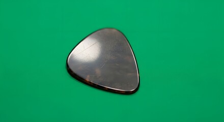 A close-up of a metallic guitar pick resting on a vibrant green background, highlighting its smooth, reflective surface and triangular shape