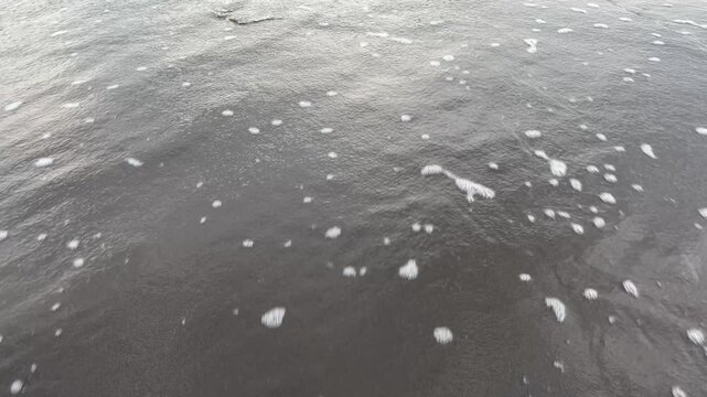 a gentle ocean wave washing over a dark sandy shore, creating foam patterns and textured water. natural beach scene with calm movement and simple composition