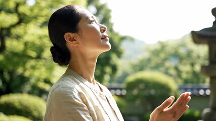 An Asian woman praying with her hands together in a traditional Japanese garden. A middle-aged person meditating and showing gratitude outdoors. Spirituality and mindfulness concept