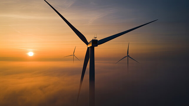 Wind turbines silhouetted against a sunset sky with a layer of fog at the horizon line view - Powered by Adobe