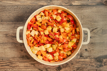 Colorful vegetable medley being prepared in a large pot on a wooden surface
