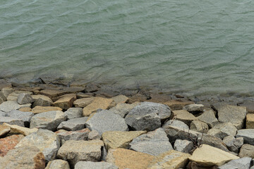 rocky shoreline with gentle water ripples, natural stones meeting calm greenish lake surface, serene outdoor landscape detail with soft textures 