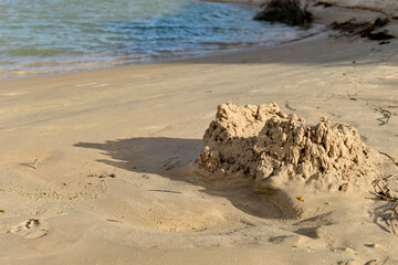 small sandcastle on tropical beach, blurred background of river and sky, summer fun concept, close up of handmade sand fort, water and horizon view, childhood memories, detail of rough, cracked wet sa