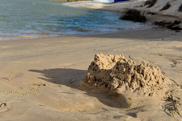 small sandcastle on tropical beach, blurred background of river and sky, summer fun concept, close up of handmade sand fort, water and horizon view, childhood memories, detail of rough, cracked wet sa