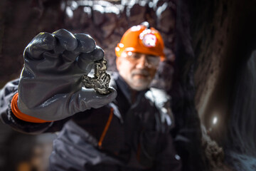 Man in a hard hat with a flashlight holding metal nugget, rare earth metal. Geology, speleology, mining with a scientific approach