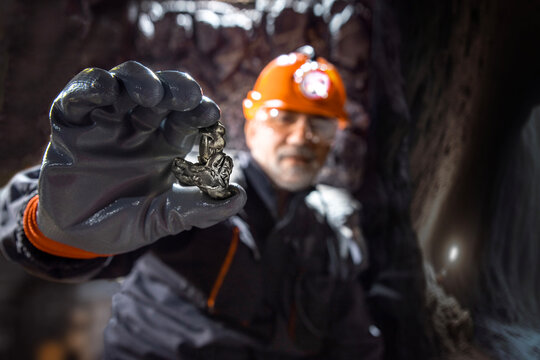 Man in a hard hat with a flashlight holding metal nugget, rare earth metal. Geology, speleology, mining with a scientific approach