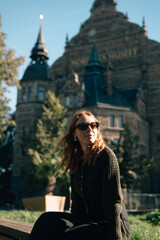 A girl wearing glasses sits near a museum in Stockholm.