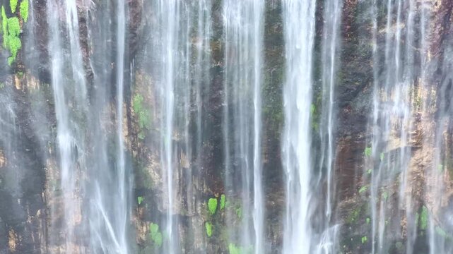 The multi-tiered Tumpak Sewu waterfall, with its lush greenery and wide stream of water flowing into a deep, semi-circular basin on the island of Java. Near Mount Semeru. Indonesia. 4К