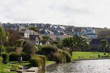 A coastal town nestled on a hillside with a lake in the foreground. Lush greenery surrounds the lake, enhancing the idyllic scenery in Perranporth - Cornwall - UK