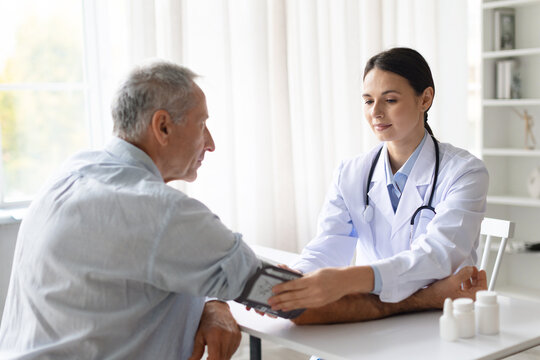 Female doctor in white coat measuring blood pressure of senior male patient during medical checkup in clinic, professional healthcare service concept