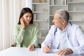 Fototapeta premium Pregnant woman feeling pain while consulting with senior male doctor in clinic, prenatal diagnosis and pregnancy discomfort healthcare concept