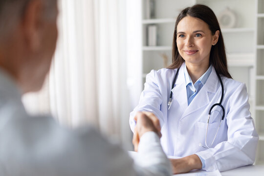 Female doctor in white coat shaking hands with senior male patient in clinic office, greeting man in hospital, professional healthcare interaction and trust concept
