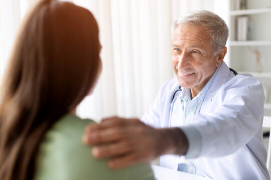 Senior male doctor reassuring female patient with supportive gesture during medical consultation in clinic office, empathy and healthcare trust concept