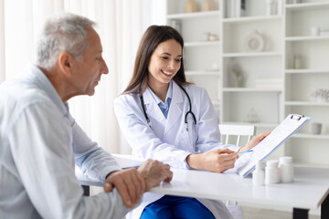Smiling female doctor showing medical document to senior male patient during consultation in clinic office, positive healthcare communication and trust concept