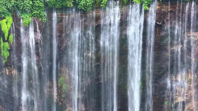 The multi-tiered Tumpak Sewu waterfall, with its lush greenery and wide stream of water flowing into a deep, semi-circular basin on the island of Java. Near Mount Semeru. Indonesia. 4К	