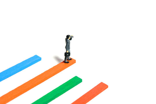 Miniature tiny people toy figure photography. Progress monitoring concept illustration. A businessman using binocular telescope standing above multiple bar chart