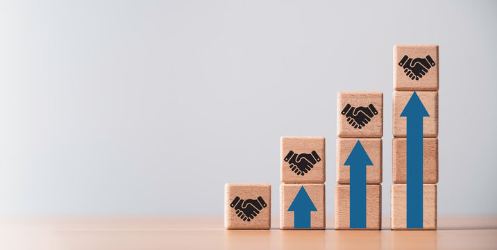 A concept of wooden blocks with handshake icons and upward arrows represent business growth partnership success teamwork development and strong collaboration ideal for corporate and financial content