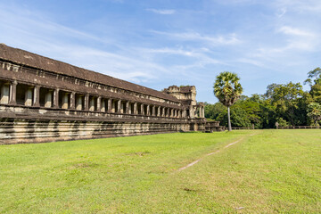 Angkor wat outer gallery shows a long stone colonnade beside a lone palm and wide grassy lawn under...