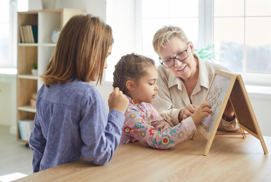 Smiling grandmother looking at her grandchildren playing with colorful geometric jigsaw, stacking puzzles into picture. Cheerful woman assisting kids with educational game during family leisure time.
