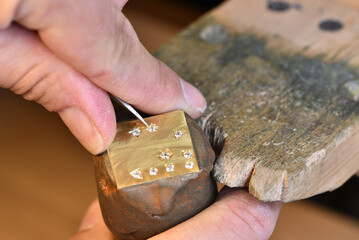A jeweler making a star setting on a gold metal plate of white round shape stones