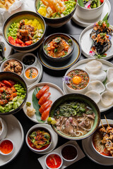 A large table with Asian cuisine. Soups, sushi, appetizers, poke bowls, shrimp, sauces