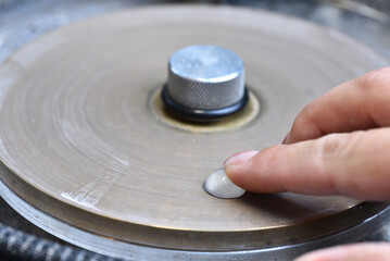Woman worker cutting a white cabochon stone on a faceting machine.