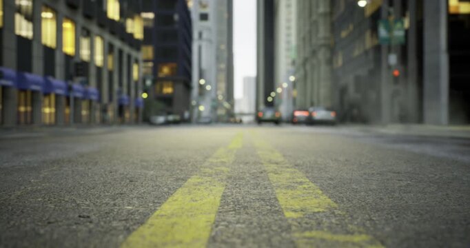 Dusk falls over a bustling city street, where vehicles move steadily along yellow lines. Buildings rise high on either side, reflecting the last light of day with windows aglow. - Powered by Adobe