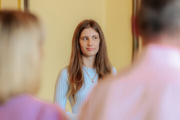 A young woman with long brown hair, dressed in a light blue dress and heart pendant, looks...