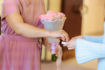 A tender moment showing a couple holding hands, both wearing wedding rings. Soft lighting and pastel clothing suggest a romantic or ceremonial occasion.