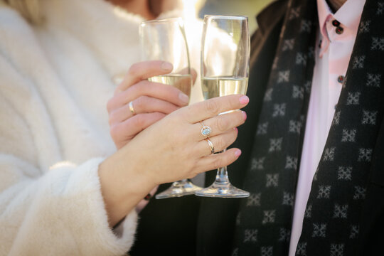 A romantic close-up of a couple clinking champagne glasses, both wearing wedding rings. The focus is on their hands and sparkling wine, suggesting celebration or engagement. - Powered by Adobe