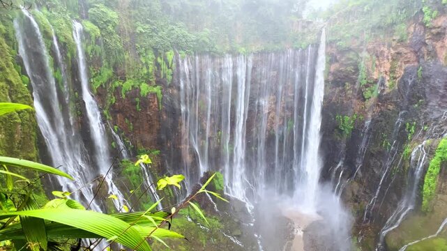 The multi-tiered Tumpak Sewu waterfall, with its lush greenery and wide stream of water flowing into a deep, semi-circular basin on the island of Java. Near Mount Semeru. Indonesia. 4К