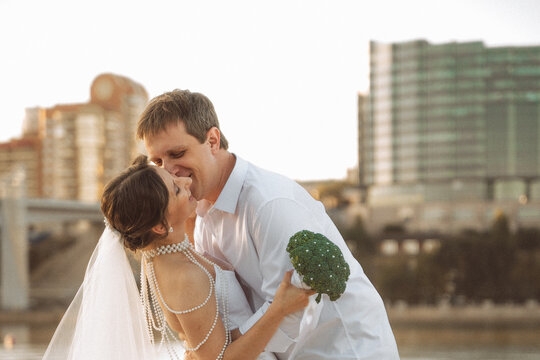 Romantic couple embracing on the beach, bride in veil holding broccoli bouquet, groom in white shirt, seaside wedding moment