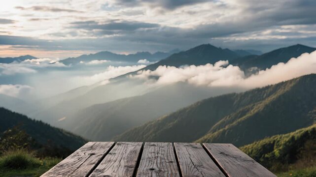 A breathtaking view of majestic mountains shrouded in clouds, with a rustic wooden table in the foreground
