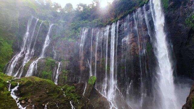 The multi-tiered Tumpak Sewu waterfall, with its lush greenery and wide stream of water flowing into a deep, semi-circular basin on the island of Java. Near Mount Semeru. Indonesia. 4К