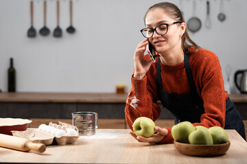 housewife talking with friend on smartphone in the kitchen at home