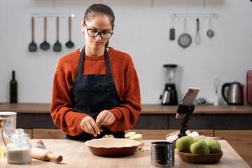 Caucasian woman preparing apple pie and recording video for social media followers