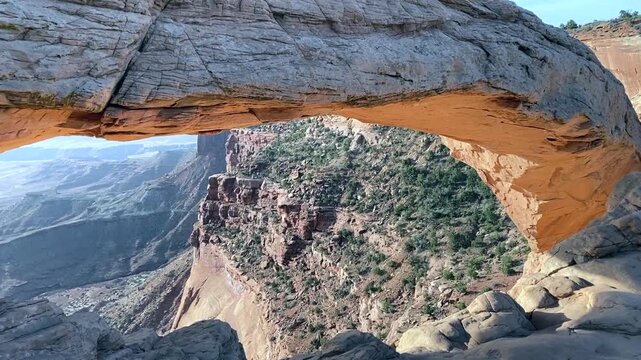Walking toward Mesa Arch in the early dawn light, the quiet desert landscape slowly awakens as soft colors glow along the rocky trail.